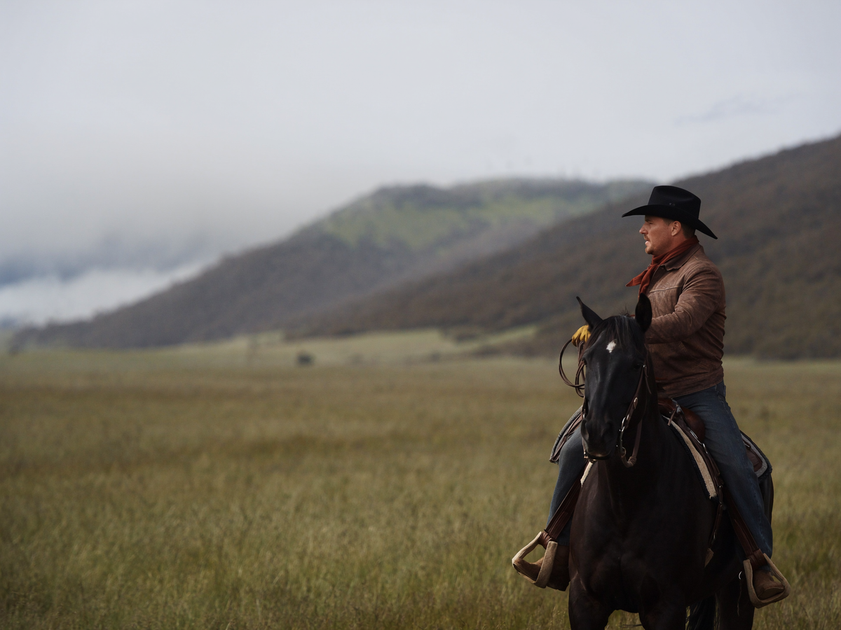 Man riding a horse in a vast open field with mountains in the background