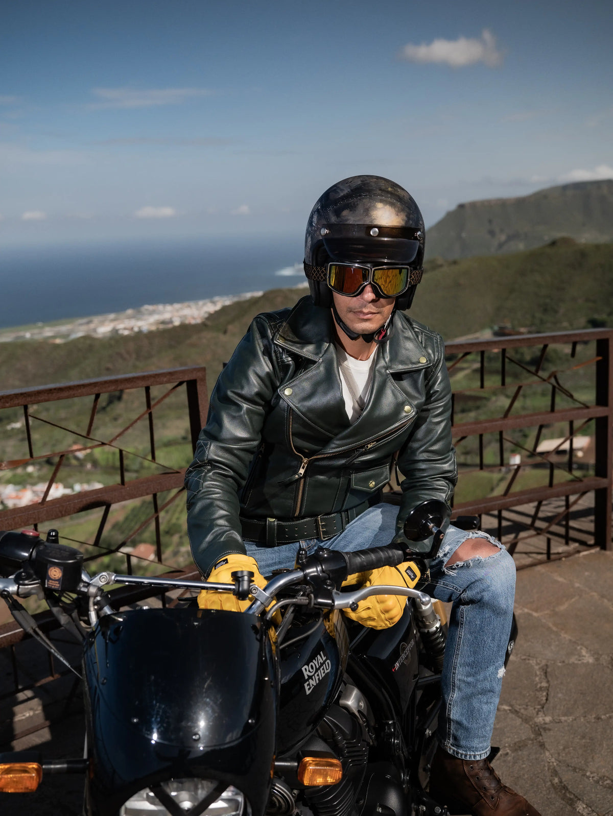 Person sitting on a motorcycle with a scenic background of mountains and ocean.