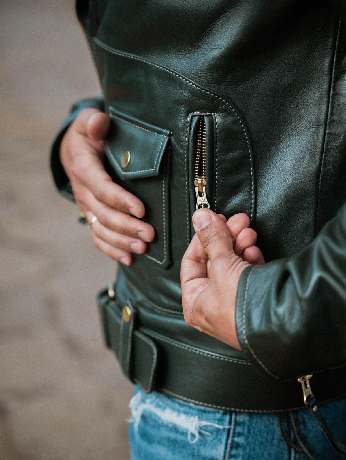Close-up of a person wearing a green leather jacket with a zipper.