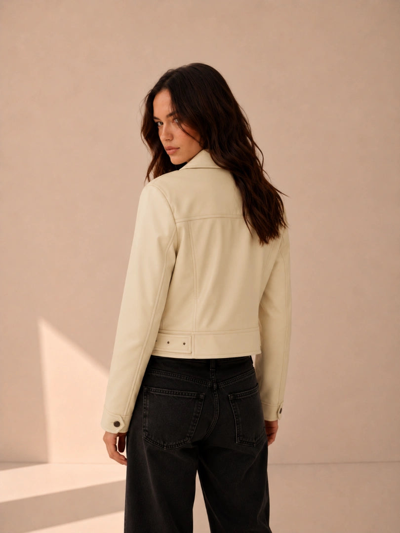 Woman wearing a light-colored jacket and dark pants against a beige background