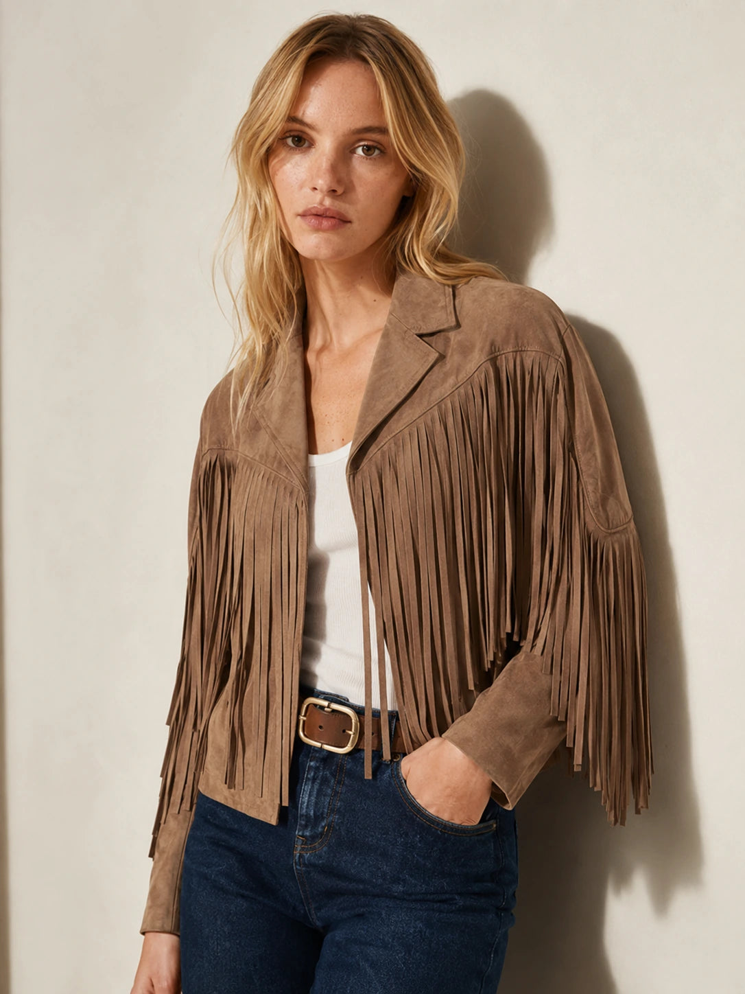 Woman wearing a brown suede fringe jacket against a plain background