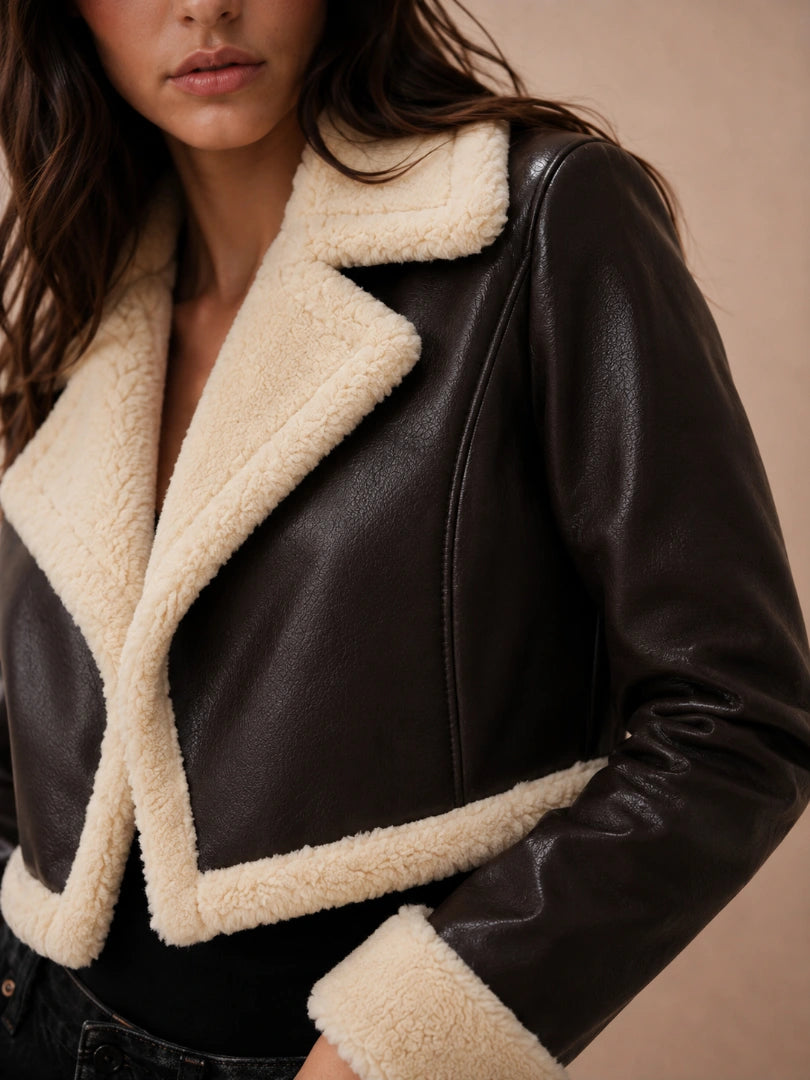 Black leather jacket with beige shearling trim worn by a person on a beige background