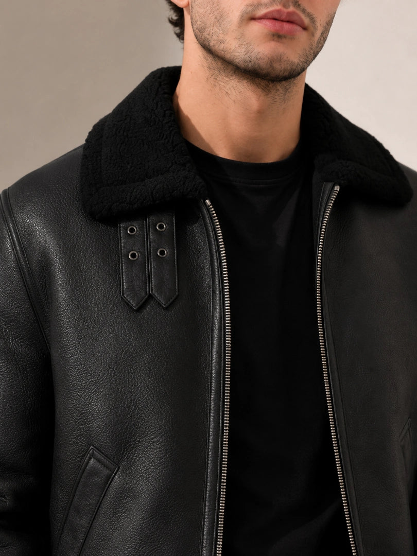 Man wearing a black leather jacket with a fur collar against a neutral background