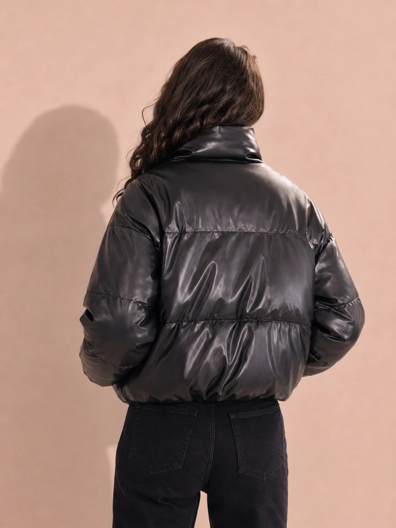 Person wearing a black puffer jacket against a beige background