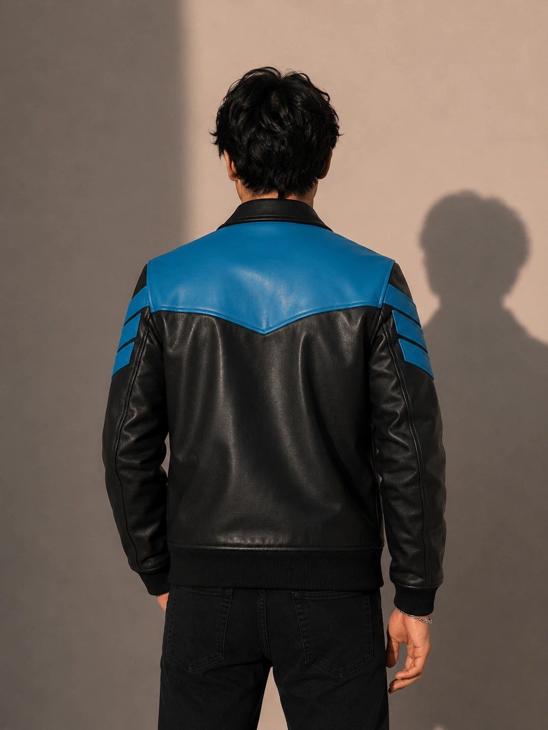 Person wearing a black and blue leather jacket against a beige background