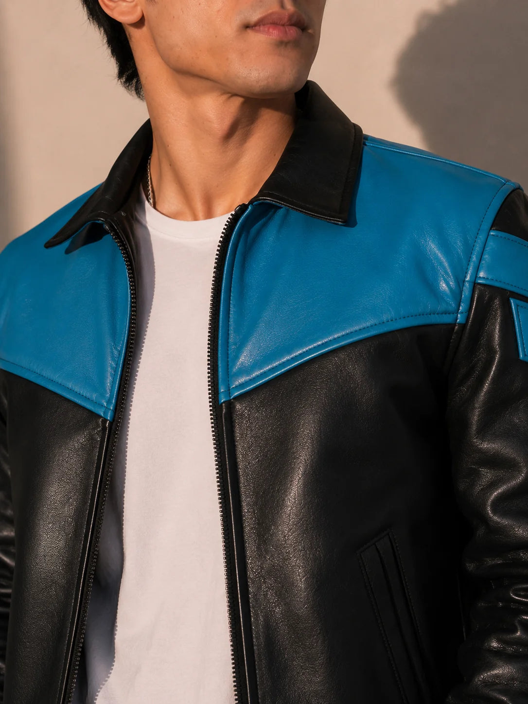 Person wearing a black and blue leather jacket with a neutral background