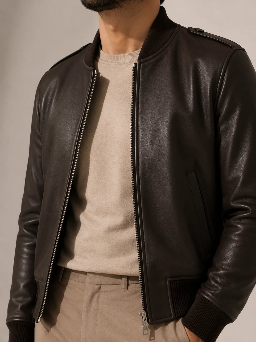 Person wearing a black leather jacket over a beige shirt and pants on a neutral background