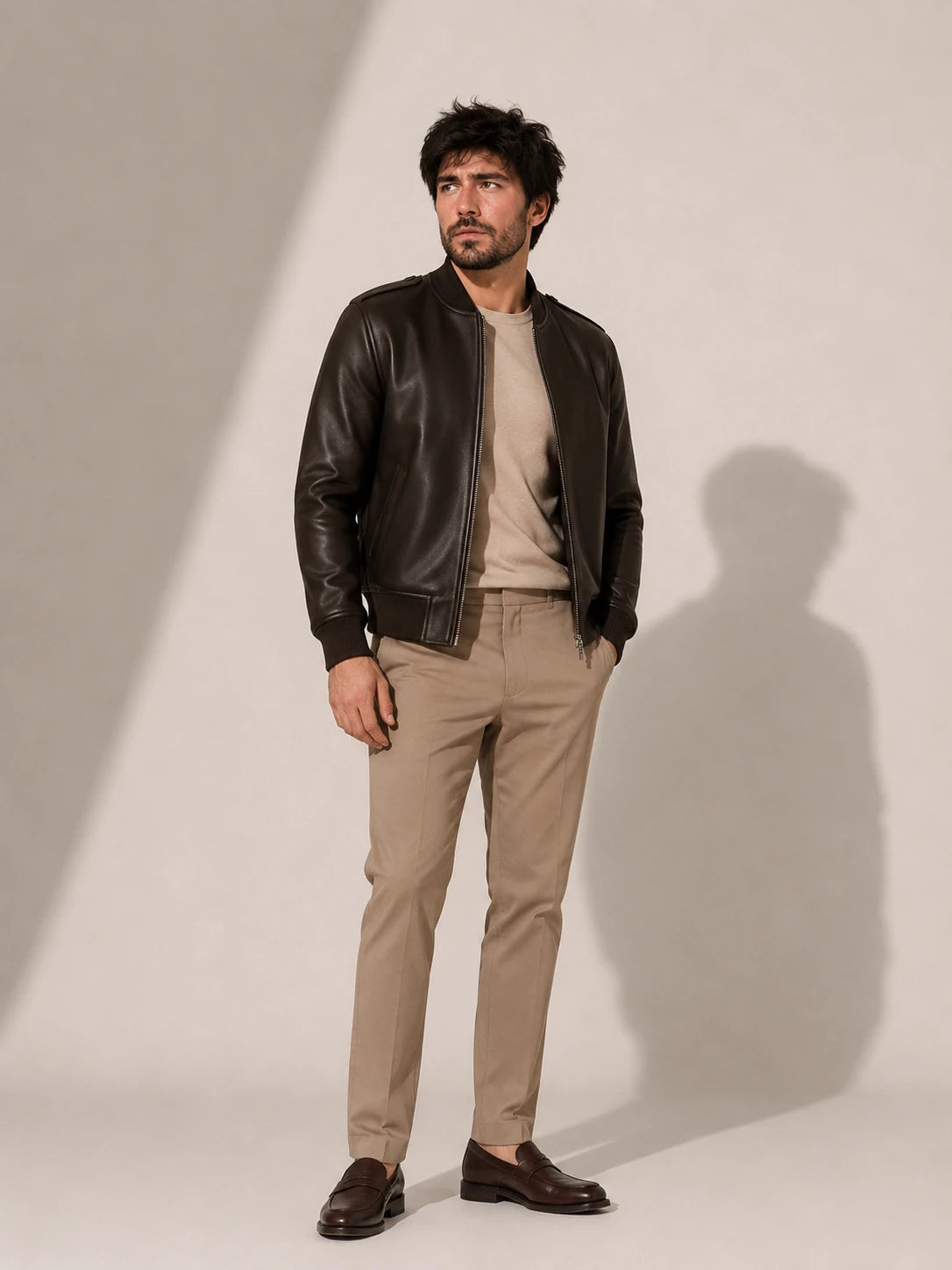 Man wearing a black leather jacket and beige pants against a plain background