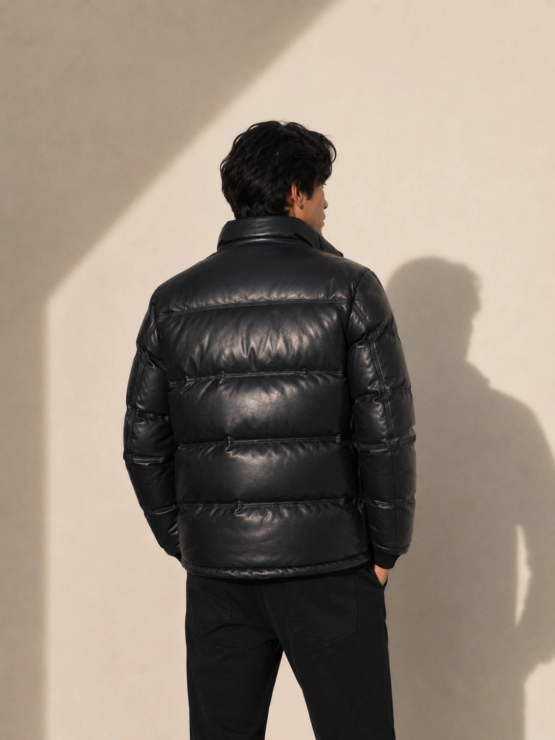 Person wearing a black puffer jacket standing against a beige wall.