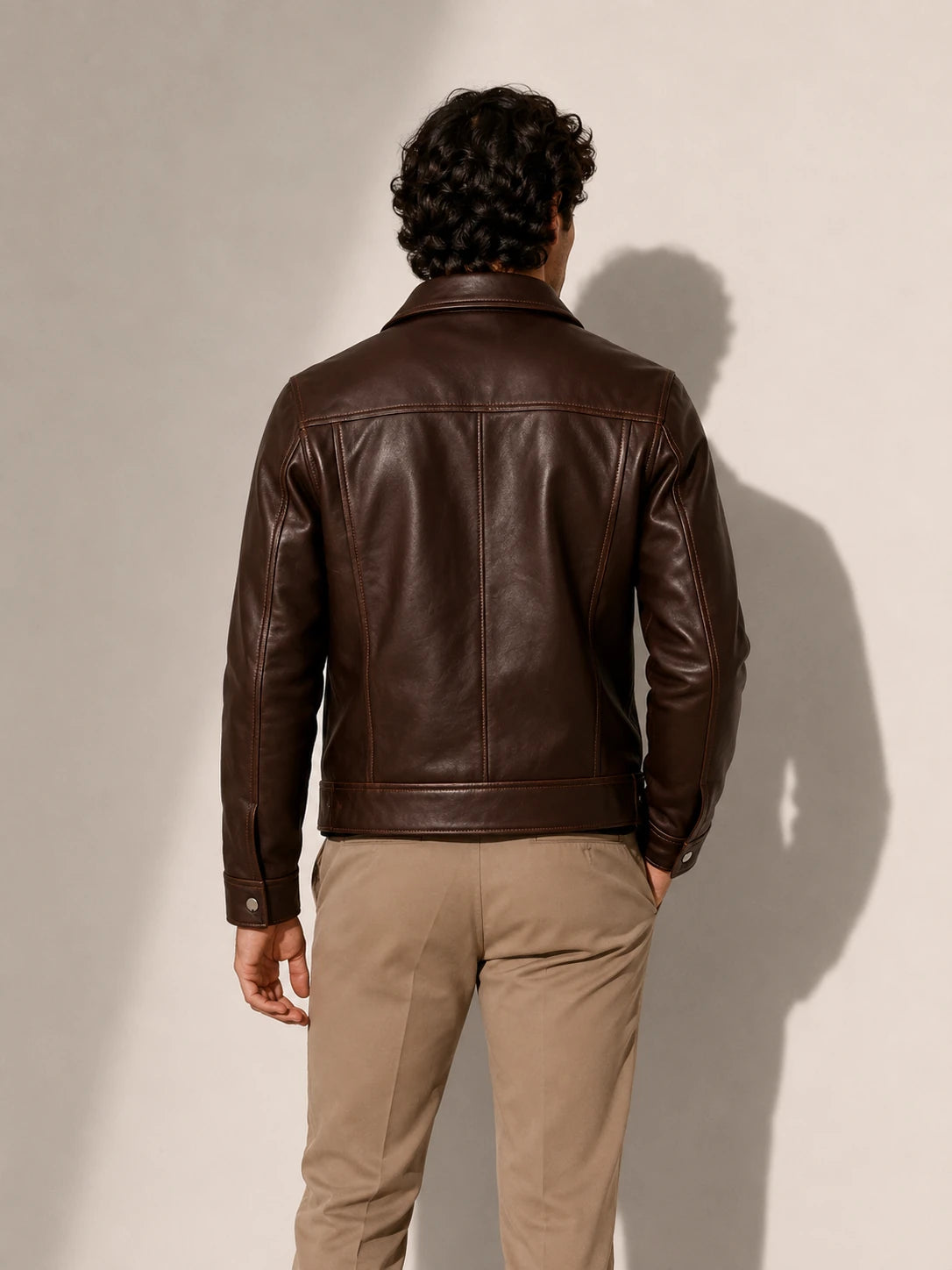 Man wearing a brown leather jacket and beige pants against a plain background