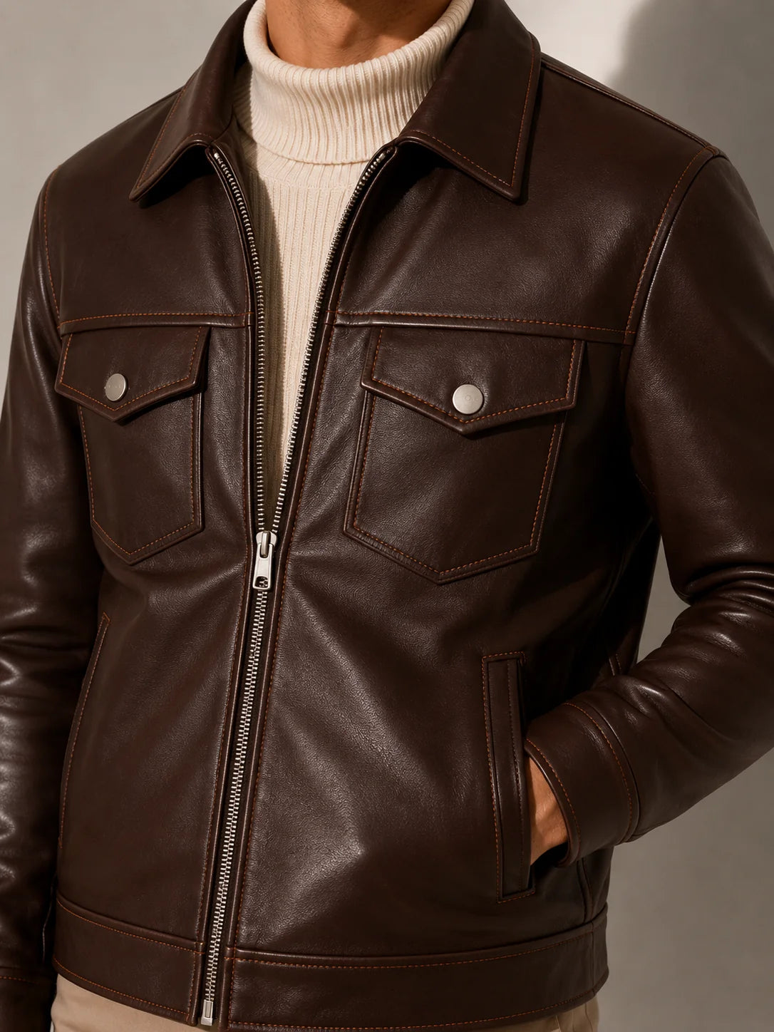 Brown leather jacket worn over a white turtleneck on a neutral background