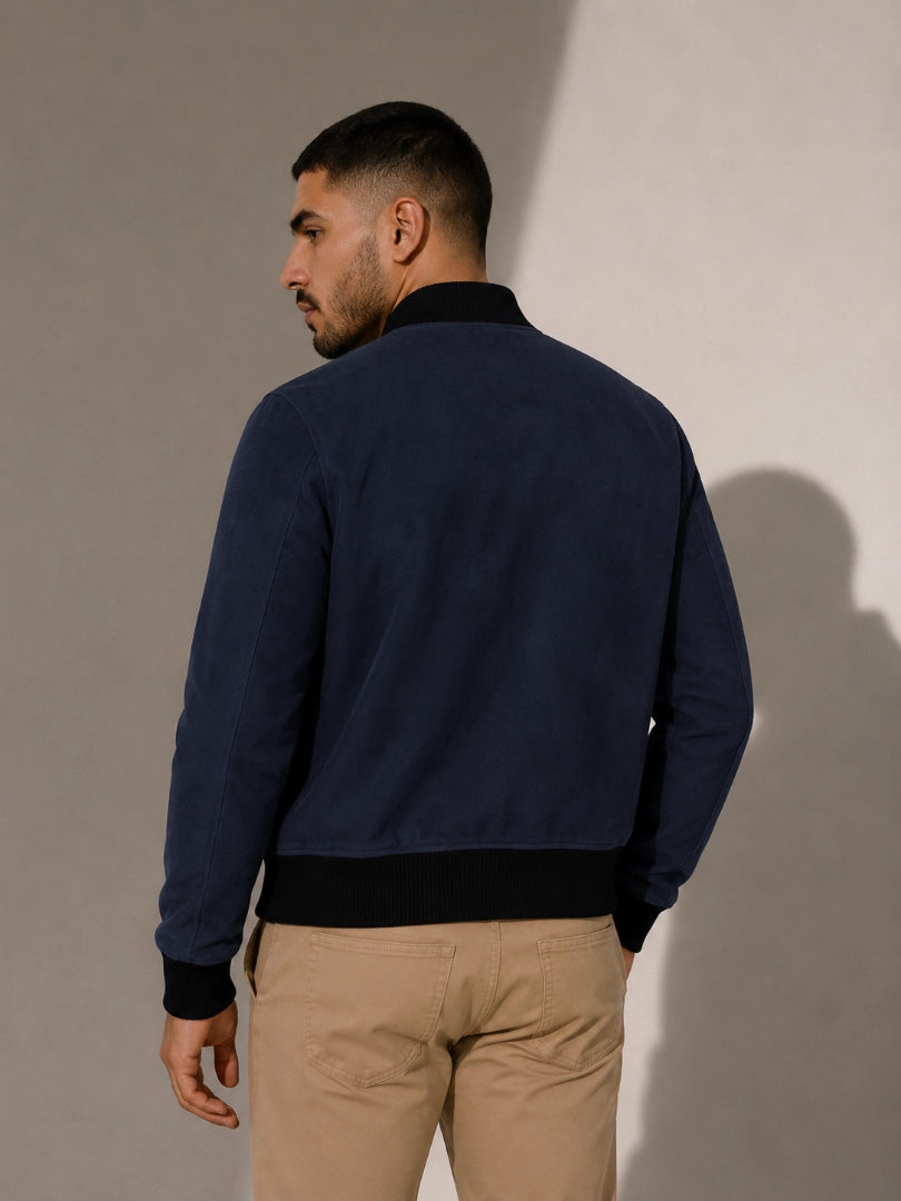 Man wearing a navy blue jacket and beige pants against a plain background