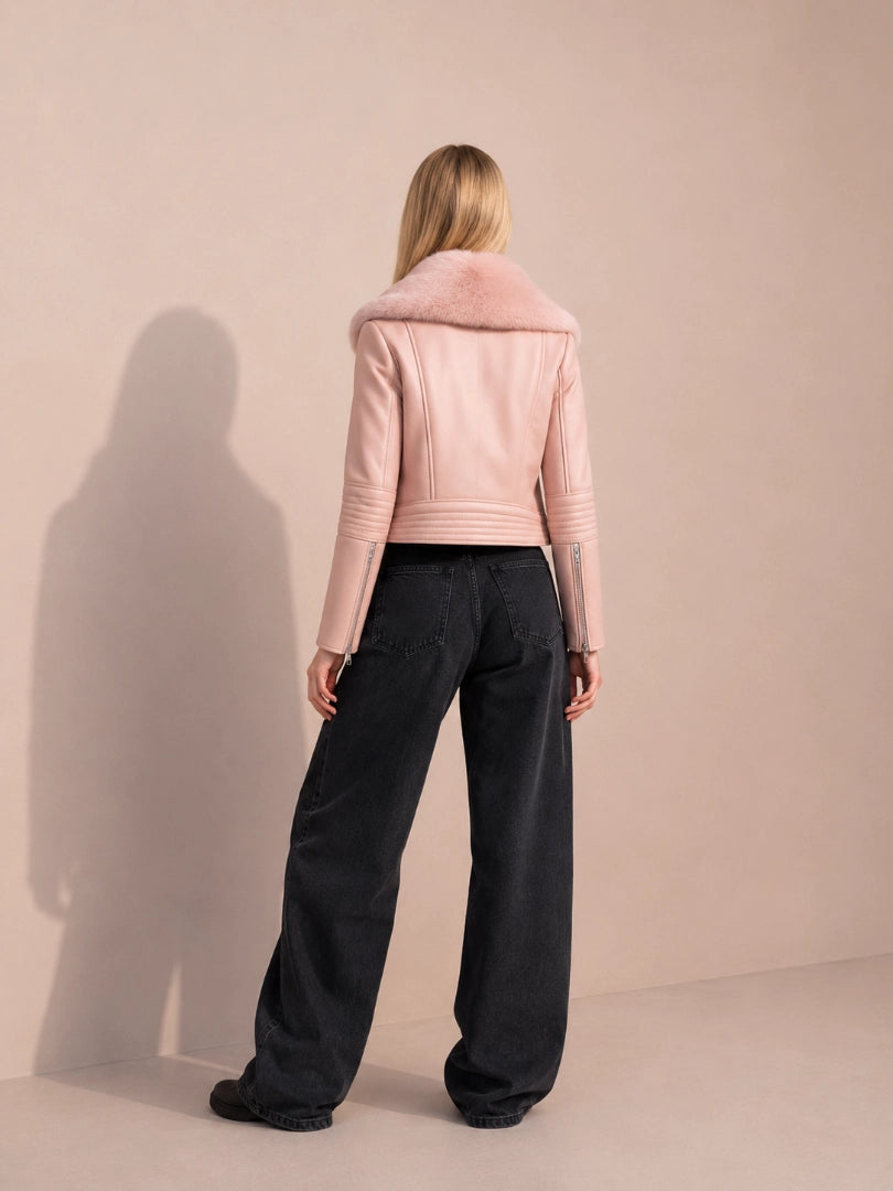 Person wearing a pink leather jacket and black pants against a beige background
