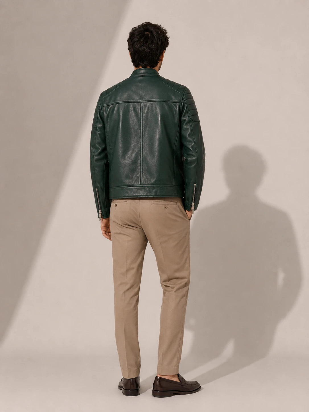 Man wearing a green leather jacket and beige pants against a plain background