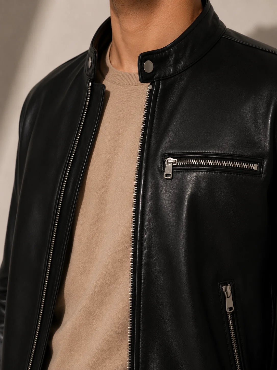 Close-up of a person wearing a black leather jacket with a beige shirt underneath.