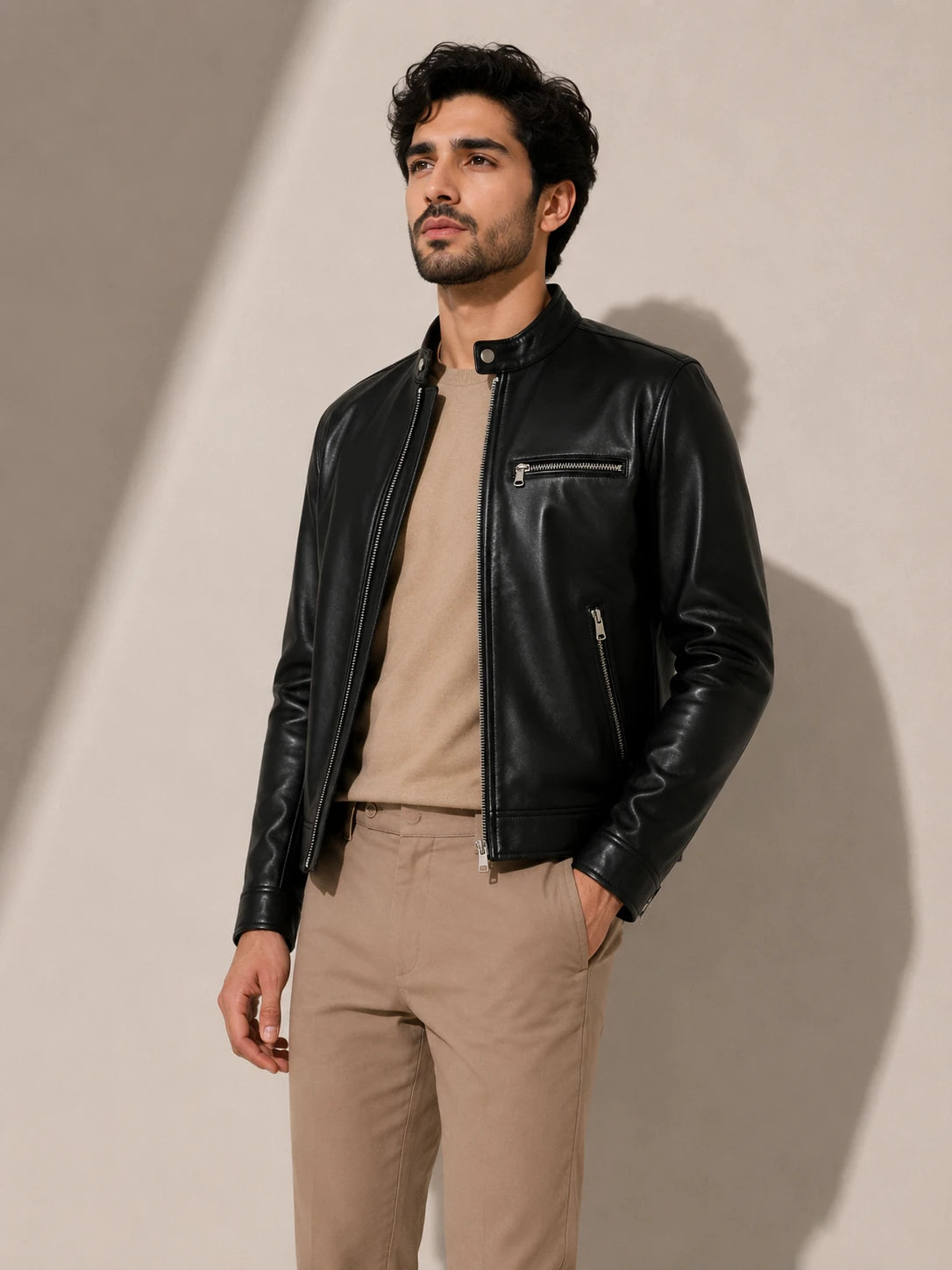 Man wearing a black leather jacket and beige pants against a neutral background