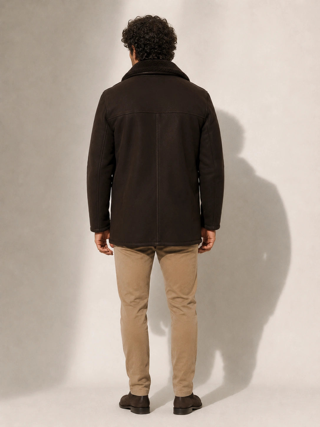 Man wearing a dark coat and beige pants against a plain background