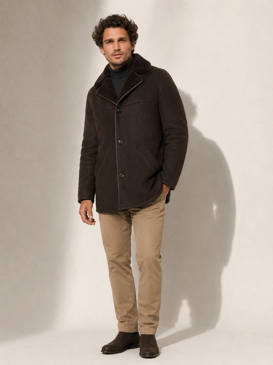 Man wearing a dark brown coat with a fur-lined hood against a plain background