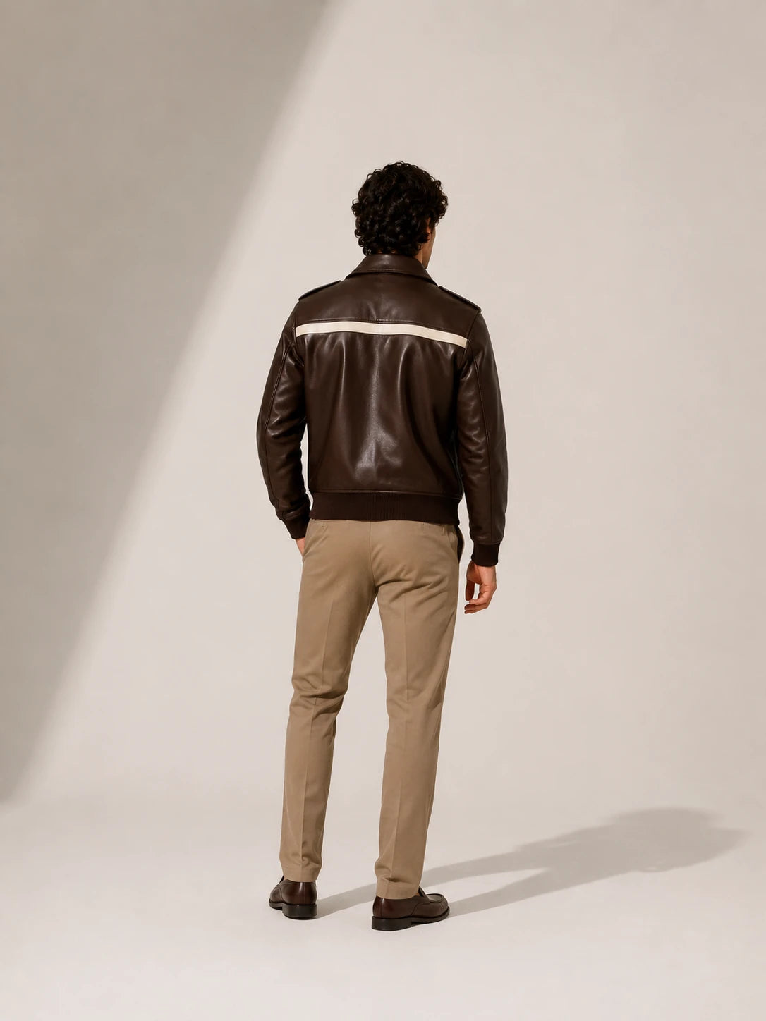 Person wearing a brown leather jacket with a white stripe on a neutral background