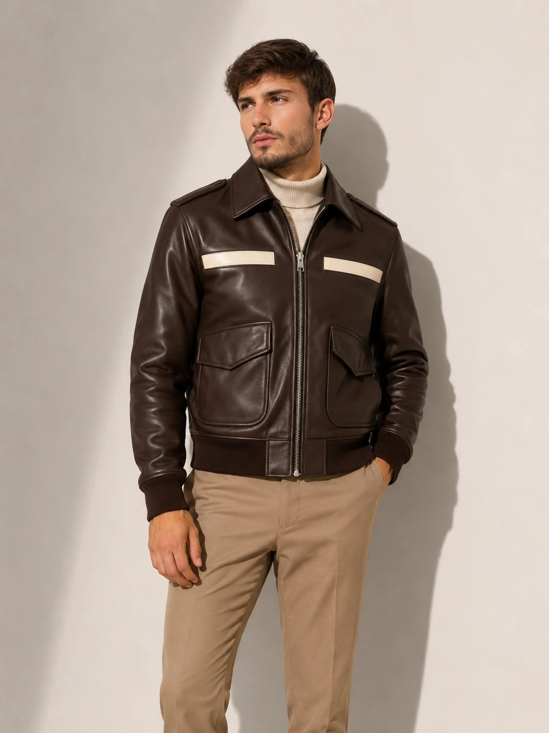 Man wearing a brown leather jacket with white stripes on a plain background