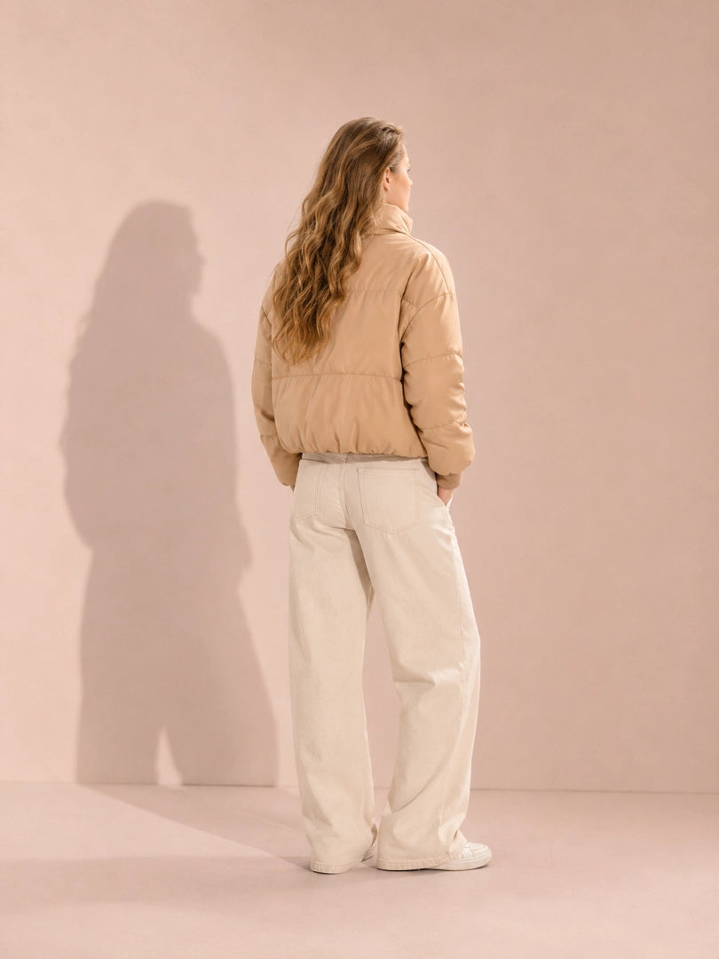 Person wearing a beige puffer jacket and light-colored pants against a plain background