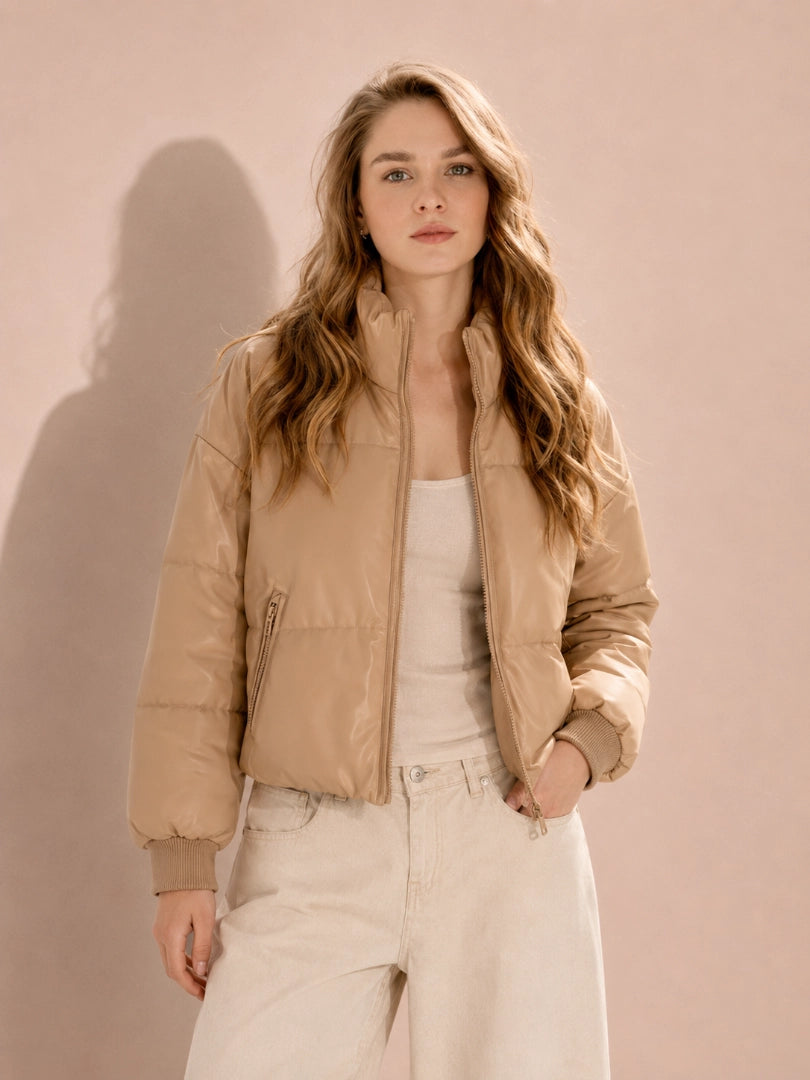 Woman wearing a beige puffer jacket against a pink background