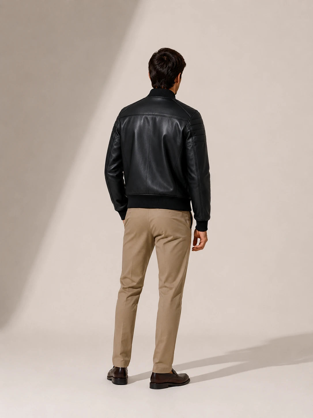 Man wearing a black leather jacket and beige pants on a neutral background