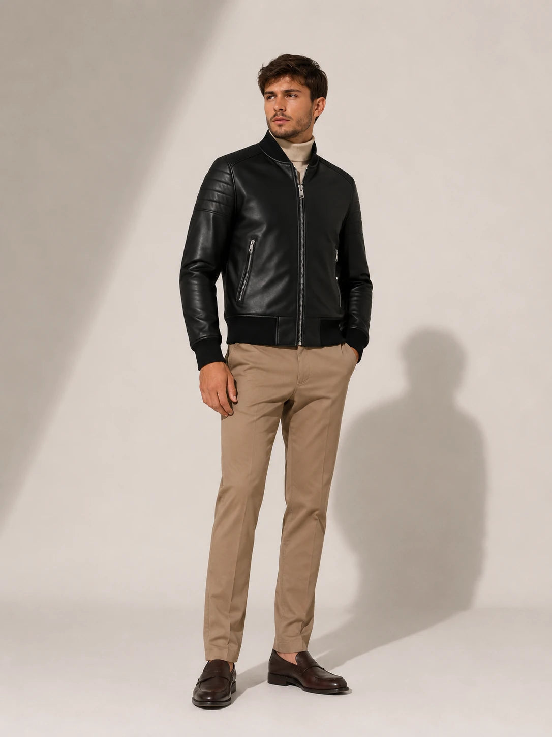 Man wearing a black leather jacket and beige pants on a white background