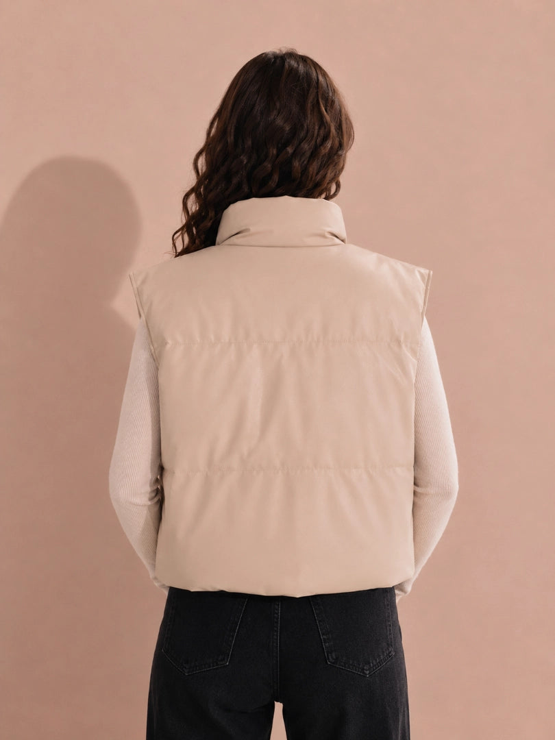 Person wearing a beige vest against a beige background