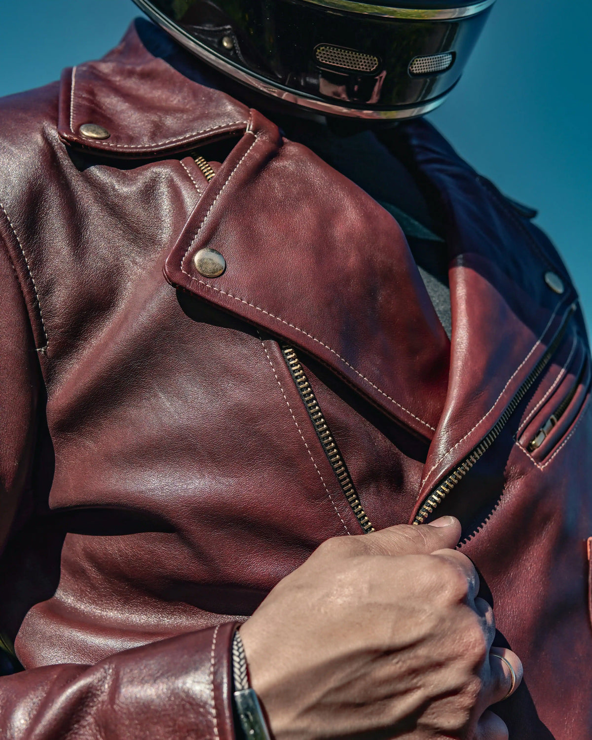 Person wearing a brown leather jacket and helmet against a blue sky.