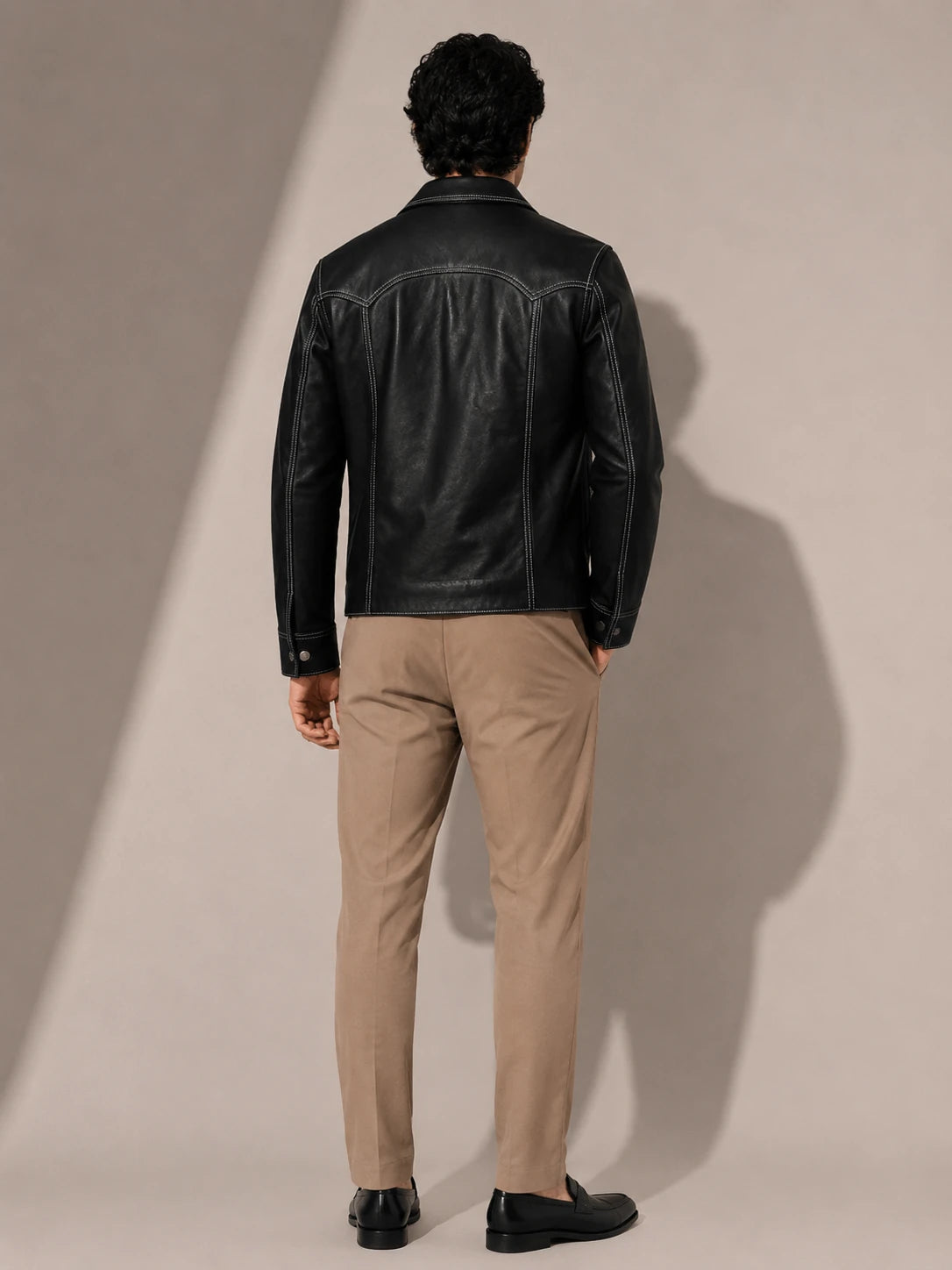 Man wearing a black leather jacket and beige pants against a plain background