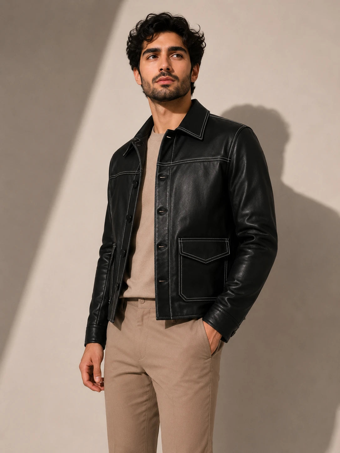 Man wearing a black leather jacket and beige pants against a neutral background