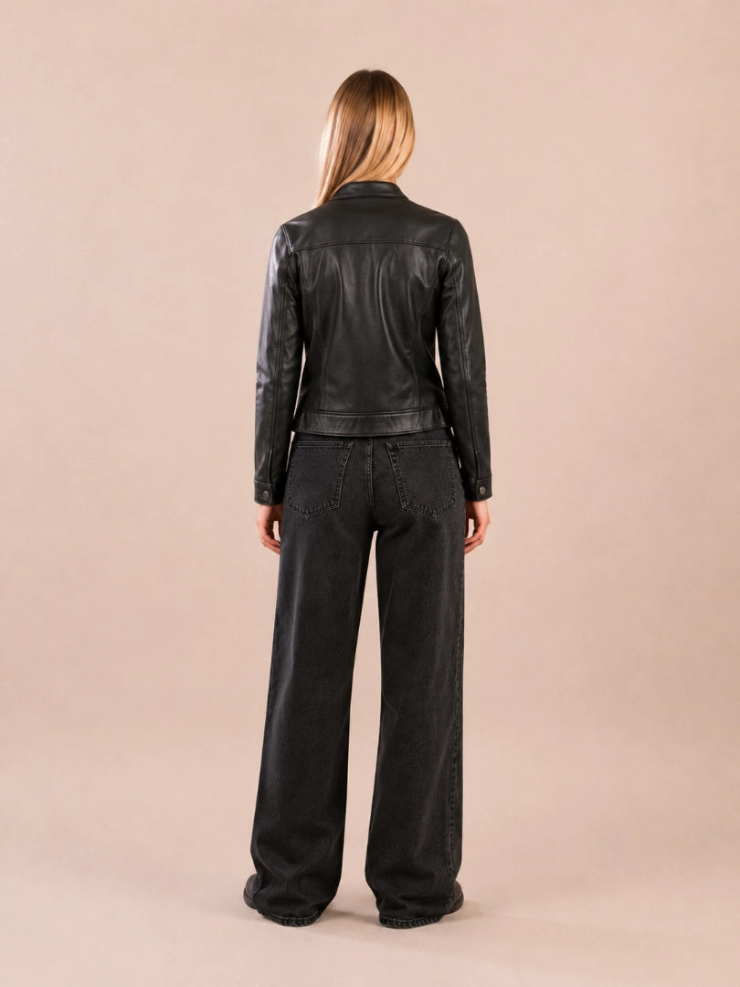 Person wearing a black leather jacket and pants on a beige background
